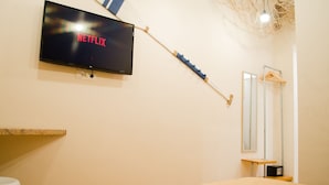 A bedroom with a TV displaying 'NETFLIX', a wooden shelf, a mirror, and a hanging light fixture. - B&B Sosta Flegrea (Naples)