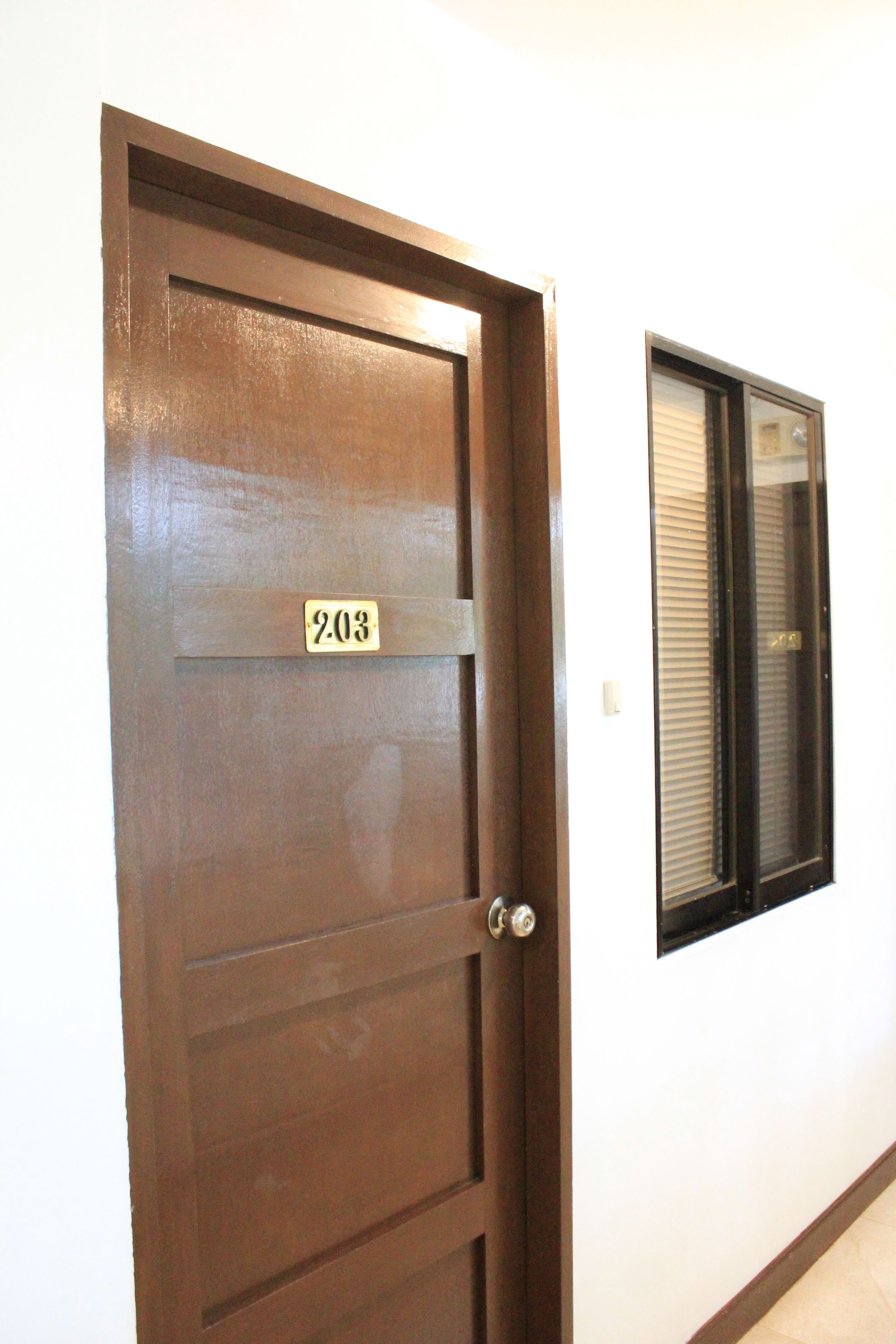 A wooden door with a number plate labeled "203" and a window with blinds to the right.