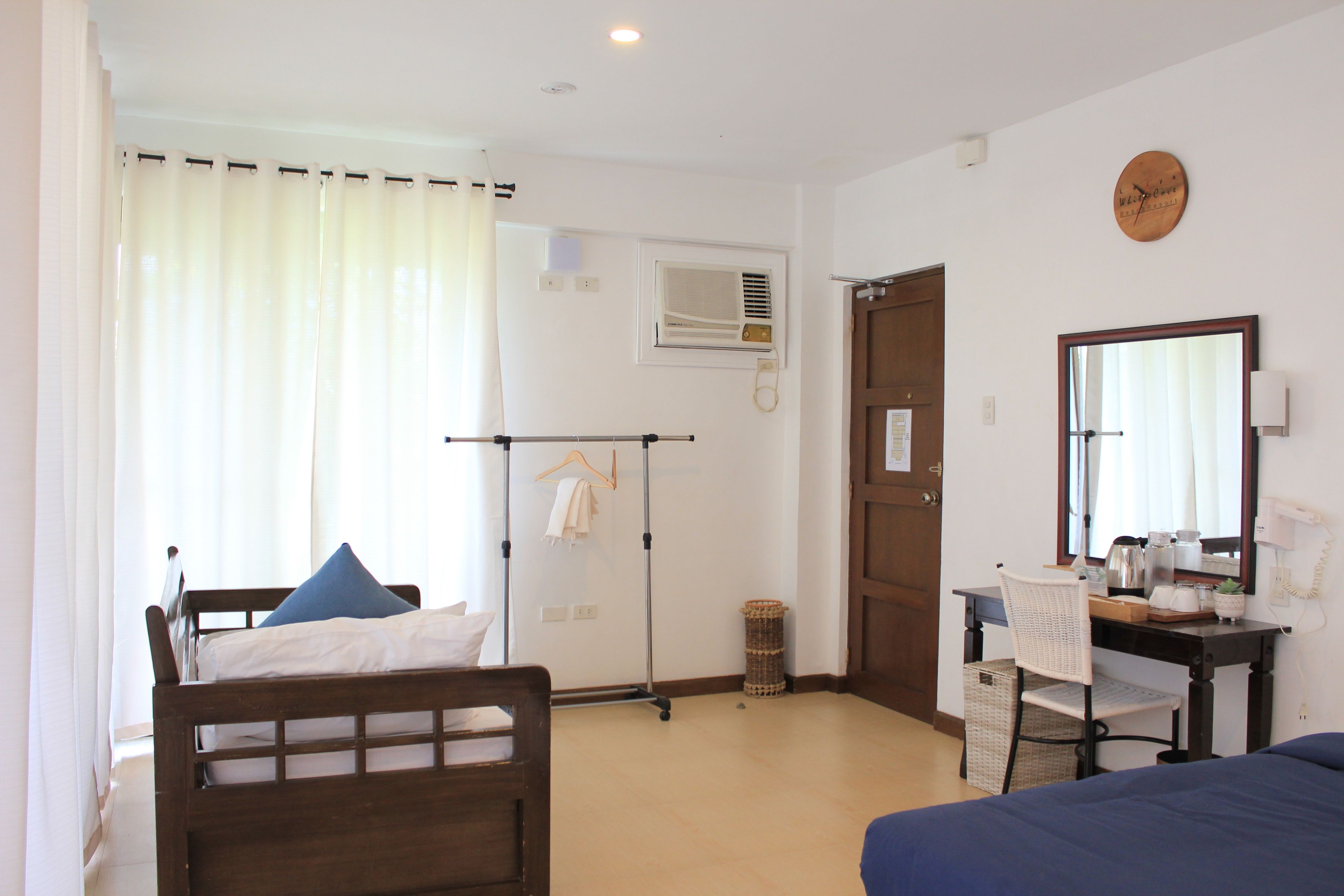 Un dormitorio con cama, escritorio, silla, espejo y ventana con cortinas.