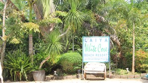 A sign for Laiya White Cove Beach Resort with a wooden bench and tropical plants.