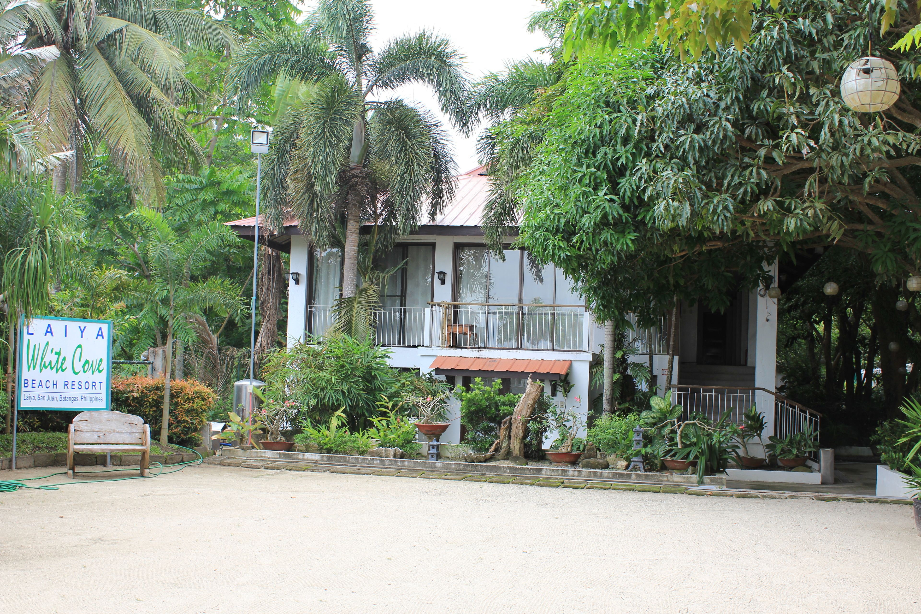 A building with a sign reading "Laiya White Cove Beach Resort" and a bench in front.