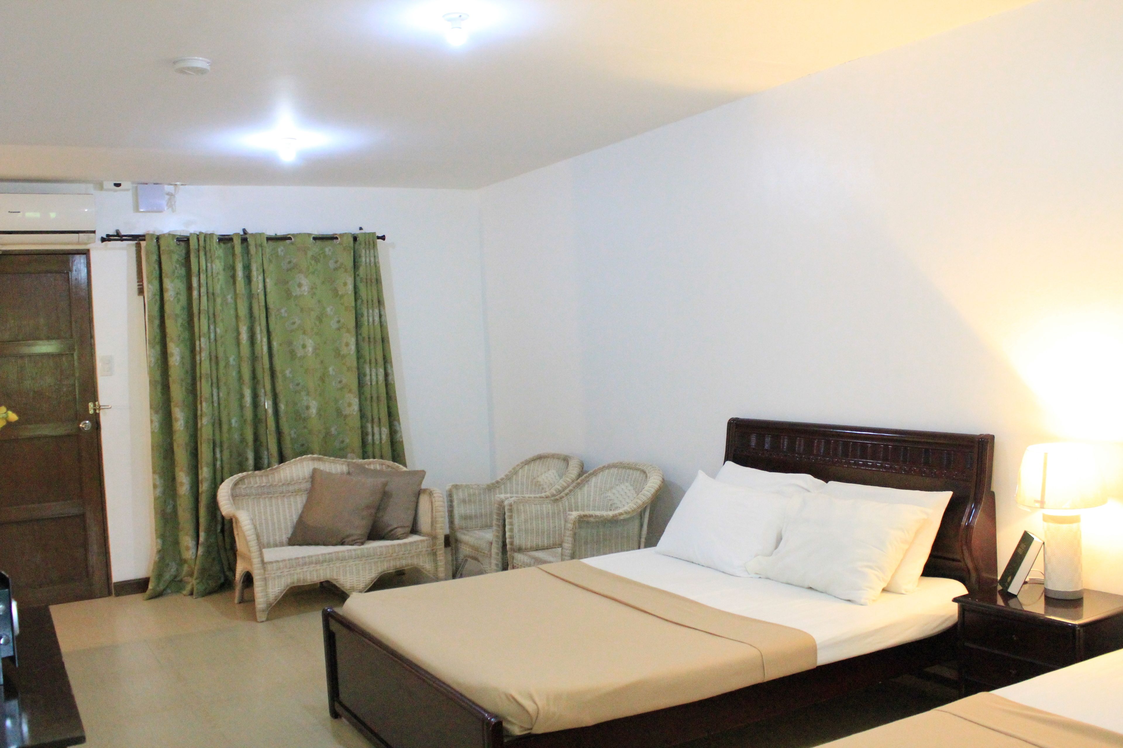 A hotel room with a bed, two chairs, a bedside table with a lamp, and a door with curtains.