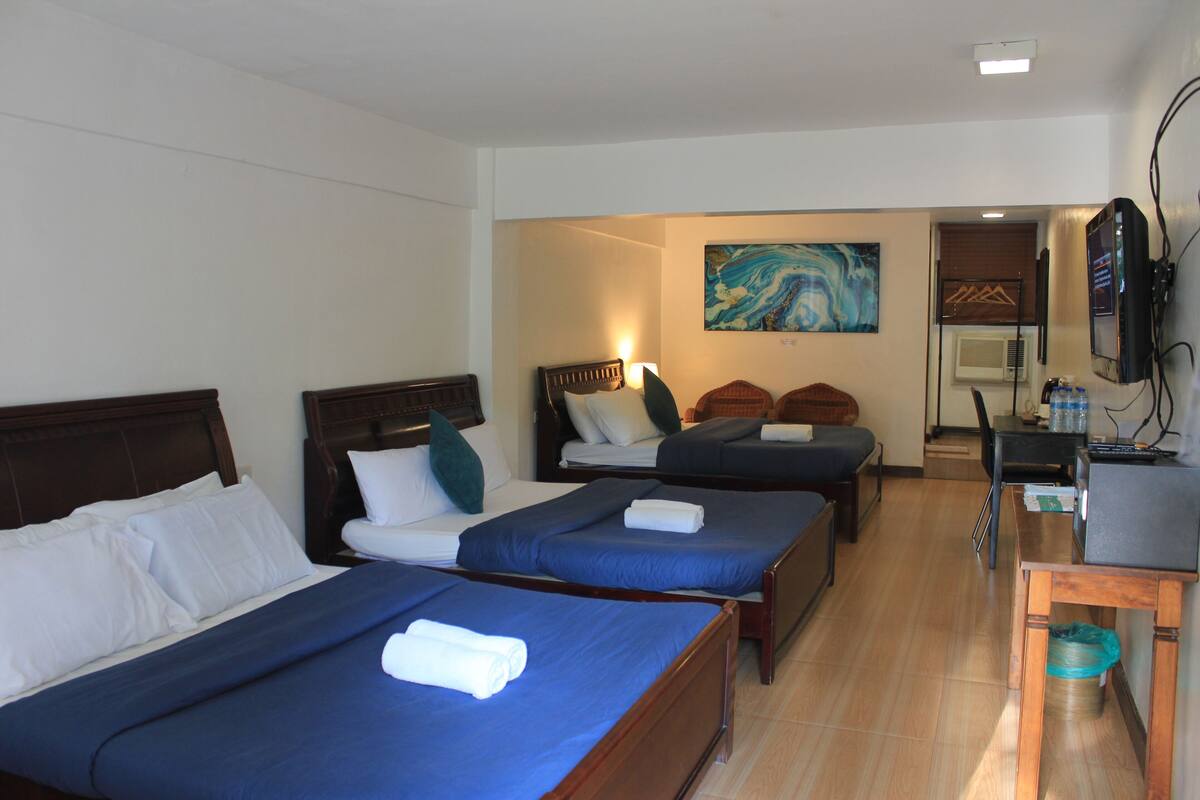 A hotel room with two single beds, a desk, a chair, a television, and a painting on the wall.