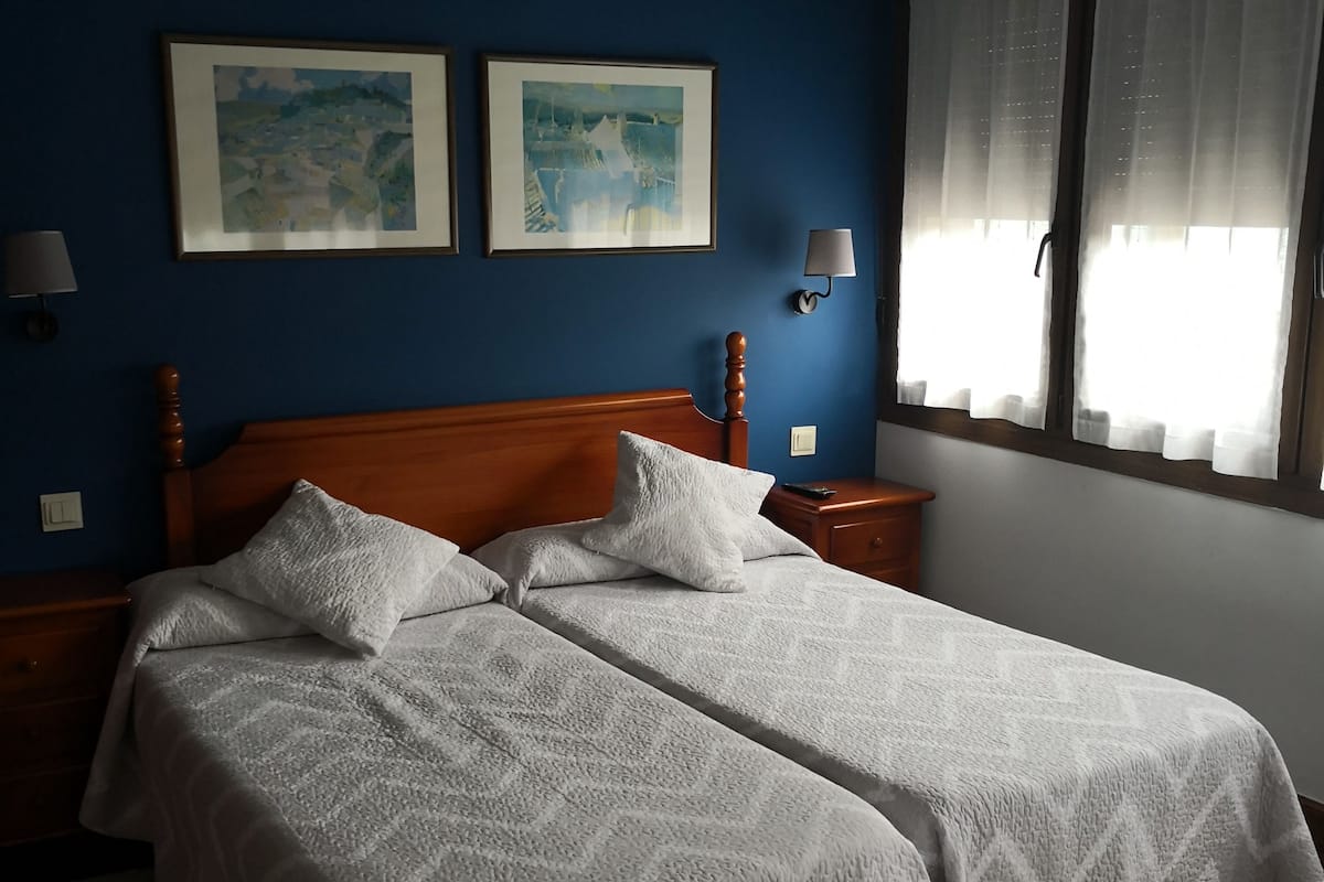 Una cama doble con cabecera de madera, dos mesitas de noche y una mesita auxiliar.