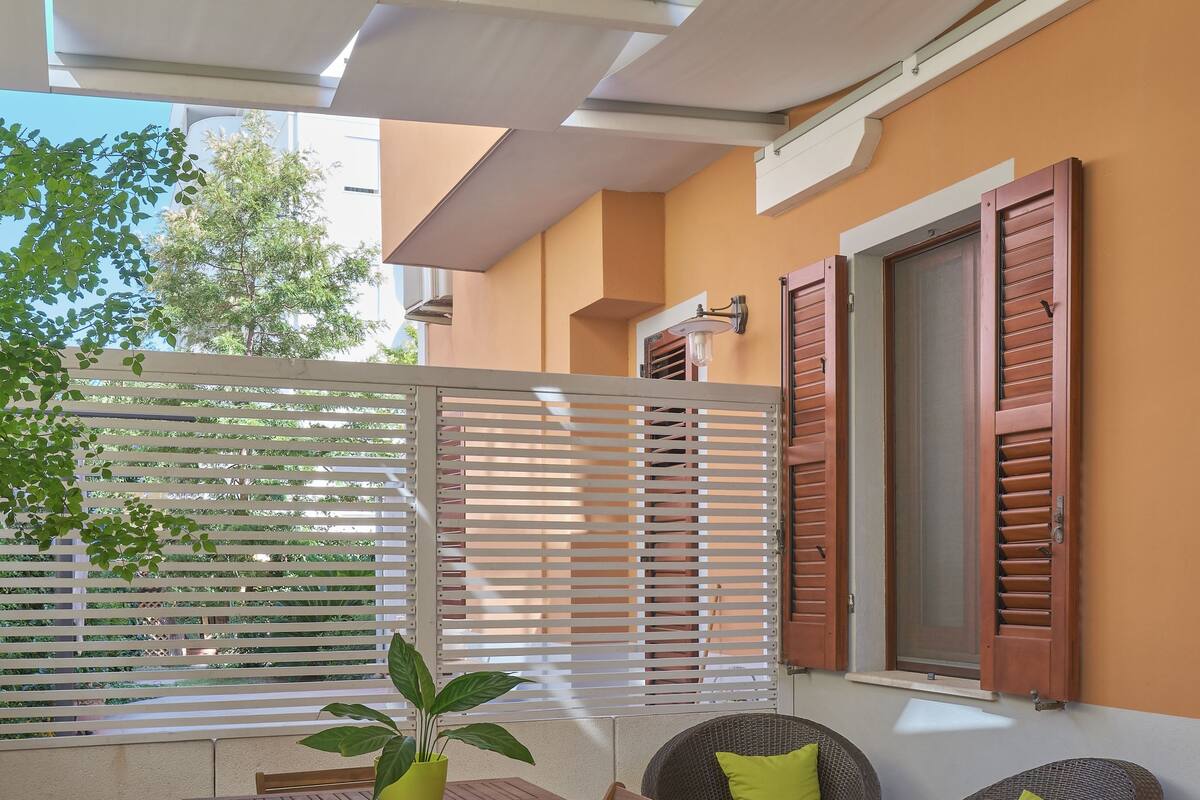An outdoor patio with a wooden table and chairs, a wicker chair, and a potted plant.
