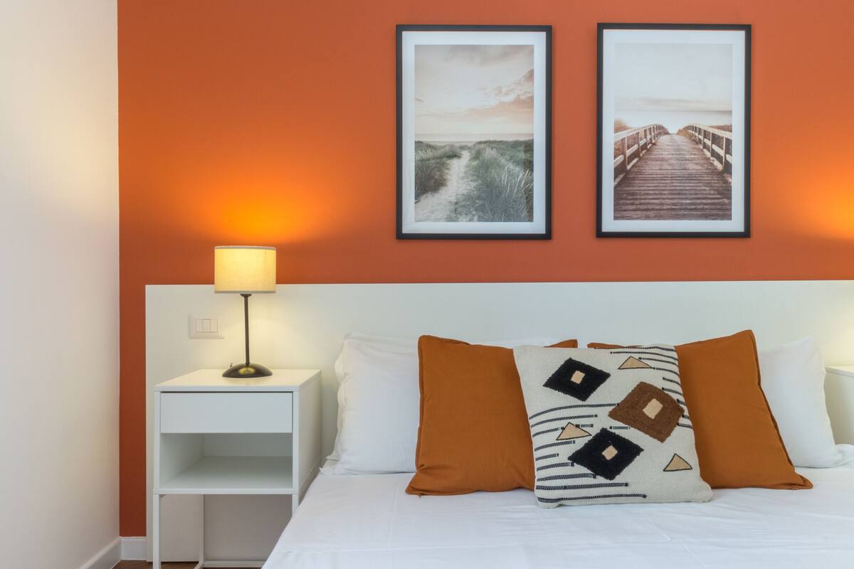 A neatly made bed with white bedding and two pillows, one with a geometric pattern.
