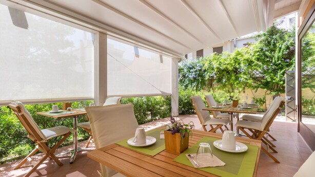 Un espacio comedor al aire libre con techado, mesas y sillas de madera, rodeado de follaje.