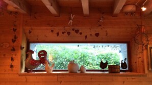 L’intérieur d’un chalet rustique, avec des murs en bois, une fenêtre donnant sur un paysage verdoyant et divers objets décoratifs disposés sur le rebord de la fenêtre.