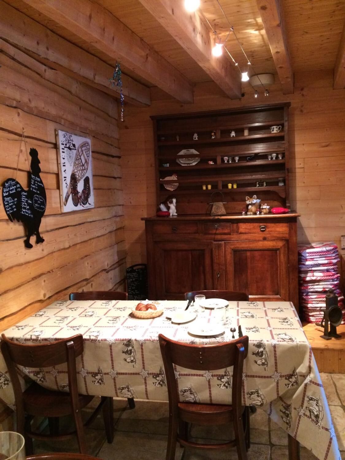 A wooden dining area with a table set for four, chairs, and a cabinet with dishes and utensils.