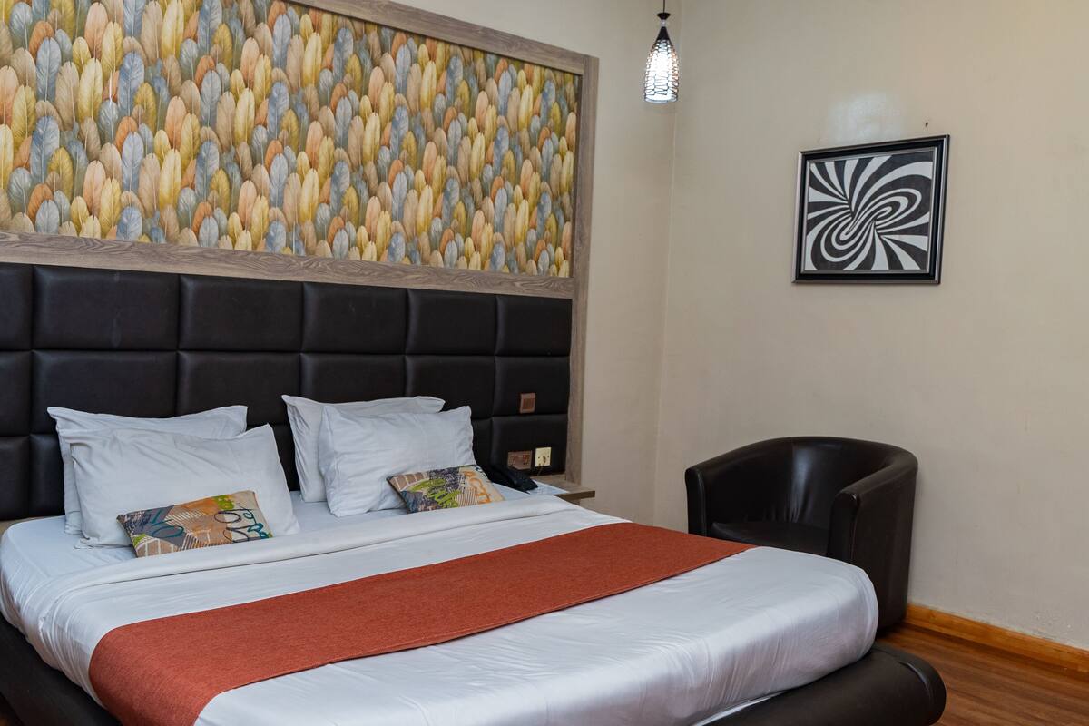 Quarto de hotel com uma cama grande, cabeceira, obra de arte na parede, arte abstrata emoldurada e uma cadeira.
