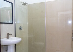 Un baño con cabina de ducha de vidrio, un lavabo blanco y un espejo.