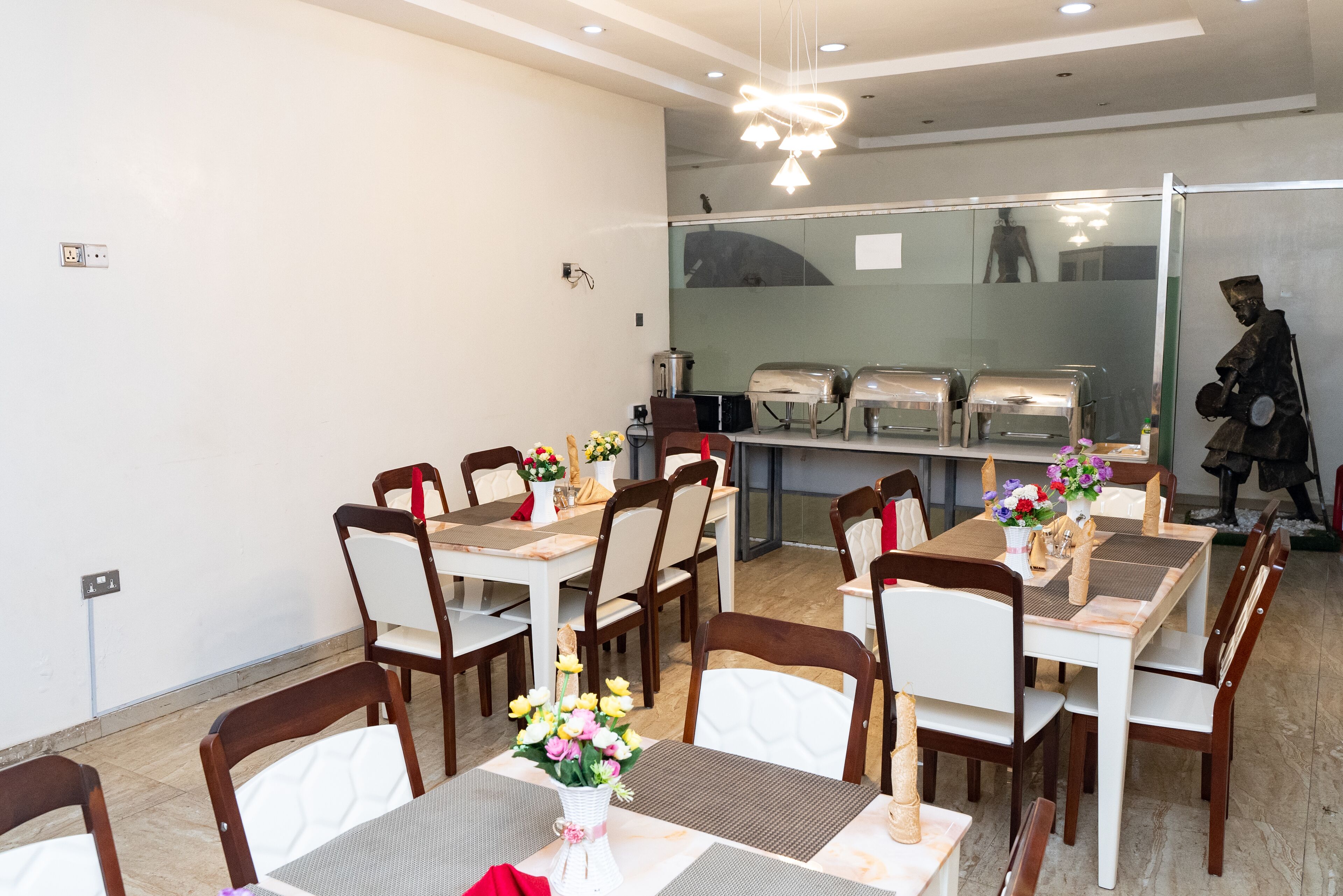 A dining area with tables set for four, each with a vase of flowers and a red napkin.