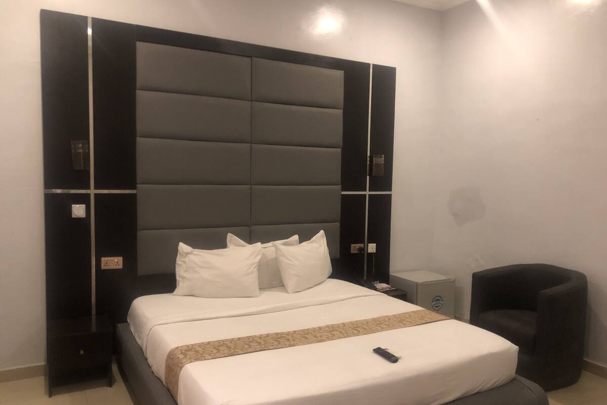 Quarto de hotel moderno com uma cama grande, uma mesa de cabeceira, uma cadeira e um criado-mudo.