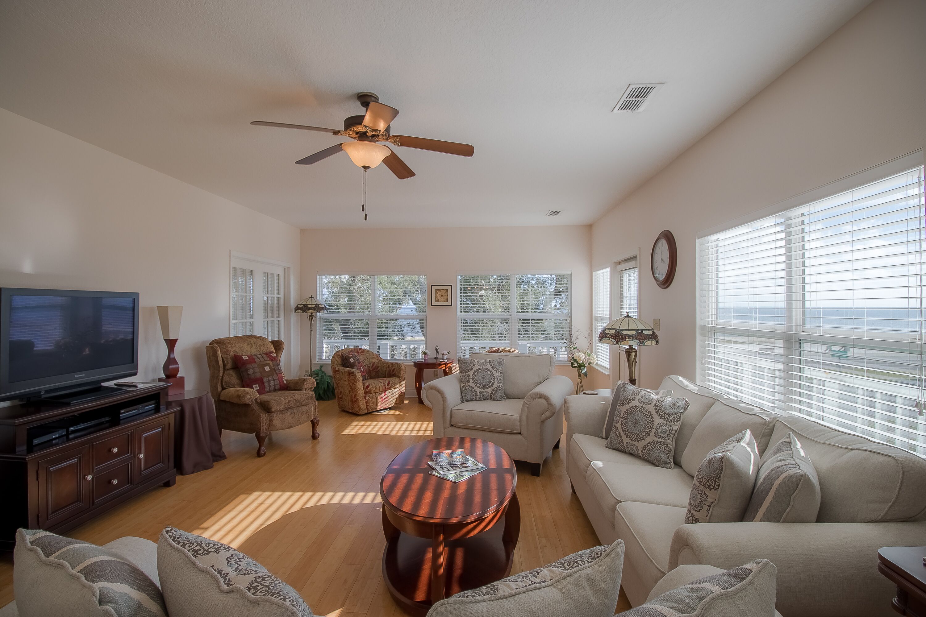 A spacious living room with a ceiling fan, a flat-screen TV, and multiple seating options including a sofa and armchairs.