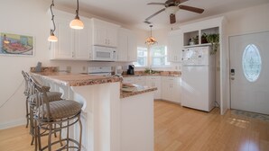 A kitchen with white cabinets, a granite countertop, a built-in microwave, a refrigerator, and a ceiling fan.