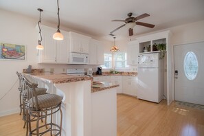 A kitchen with white cabinets, a granite countertop, a built-in microwave, a refrigerator, and a ceiling fan.