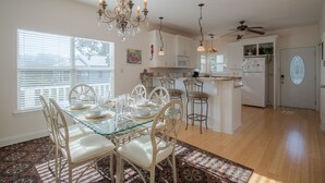 A dining area with a glass table, white chairs, a chandelier, and a patterned rug.