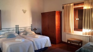 A bedroom with two beds, a wooden wardrobe, a window with curtains, a bedside lamp, and a radiator. - Sakura Vera (Villanueva De La Vera)