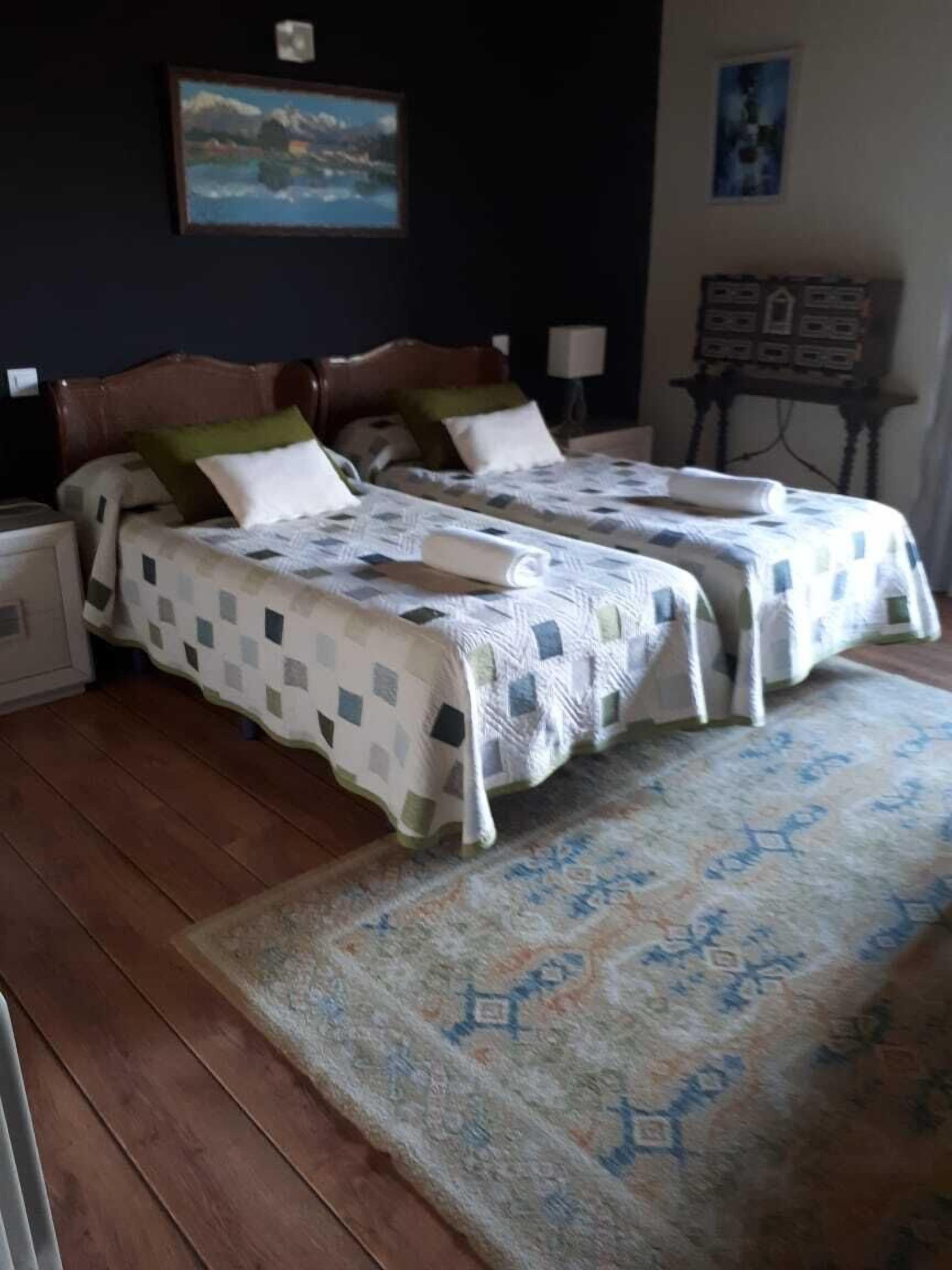 Una habitación con dos camas, una mesita de noche, una lámpara y un cuadro en la pared.