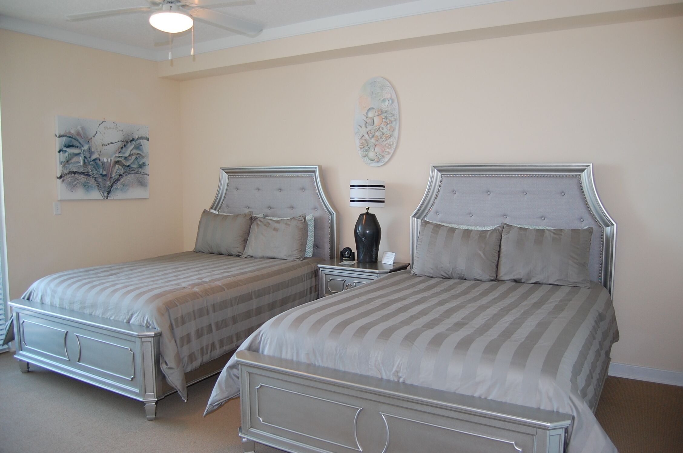 Een slaapkamer met twee bedden, een plafondventilator en kunstwerken aan de muur.
