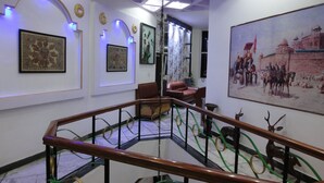 Una escalera con barandilla de madera y anillos dorados y verdes que conduce a una habitación con un cuadro de gran tamaño de una escena histórica.