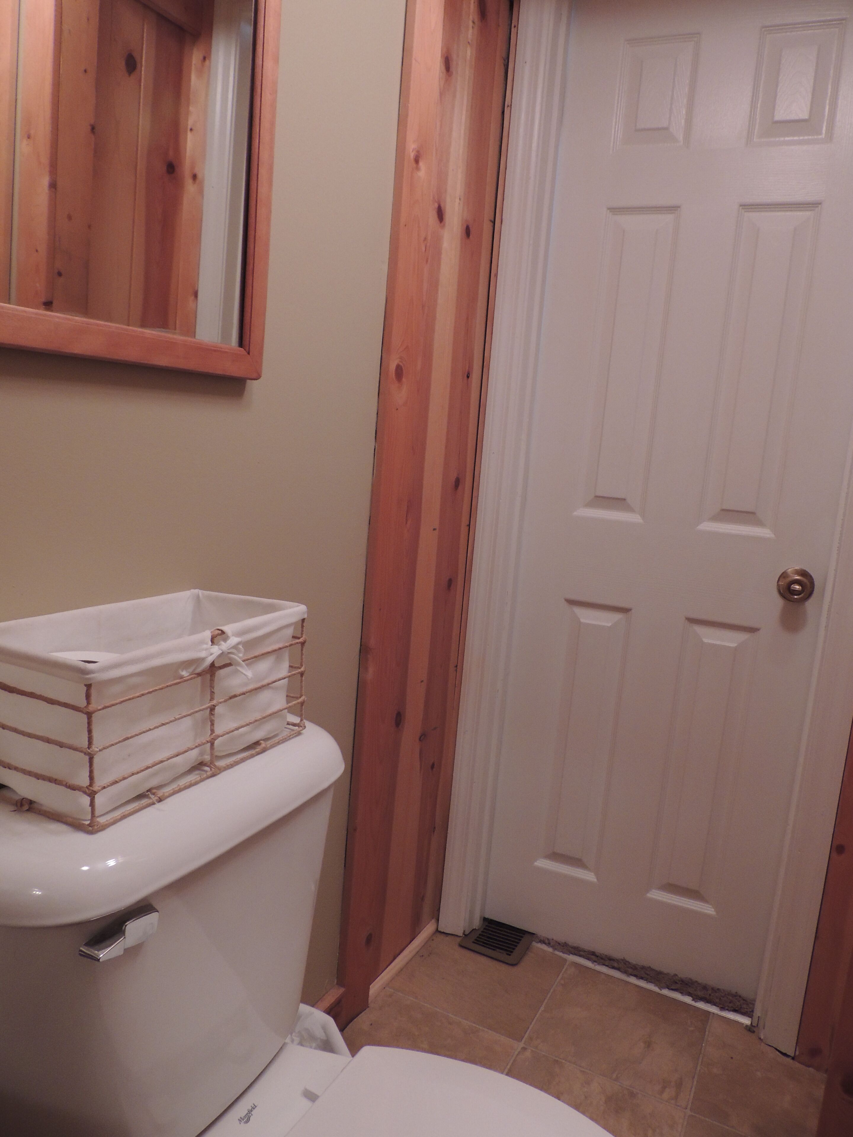 Een badkamer met een wit toilet, een houten deur en een spiegel aan de muur.