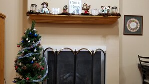 A room with a Christmas tree, a fireplace, a mantel with decorations, and a framed quote on the wall.