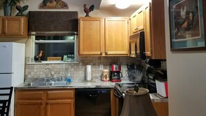 A compact kitchen with wooden cabinets, a dishwasher, a stove, and a coffee maker.