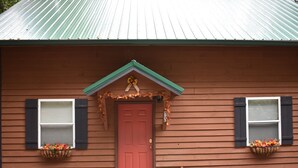A wooden building with a red door, two windows with shutters, and flower baskets on the windowsills.