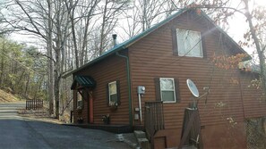 Cozy cabin with a front porch and satellite TV, nestled among trees.