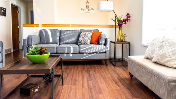 Ein modernes Wohnzimmer mit einem grauen Sofa, einem kleinen Tisch mit einer grünen Schale, einer Lampe und einer Blumenvase.