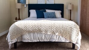 Ein ordentlich bezogenes Bett mit einer weißen und beigen Decke, zwei Kissen und einem dunkelblauen Kopfteil.
