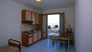 A compact room with a kitchenette, a dining area, and a view through an open door. - Residence Club Azzurro (Massignano)
