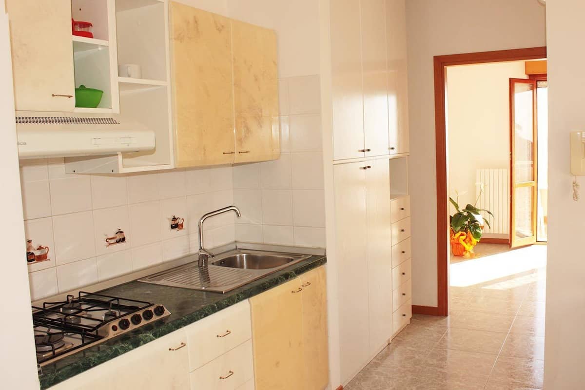 Keittiössä on valkoiset kaapit, kaasuliesi, pesuallas ja työtaso.