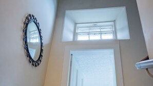 Ein Zimmer mit hohen Decken, einem großen Spiegel, einer Tür zu einem hellen Flur und einem kleinen Fenster.