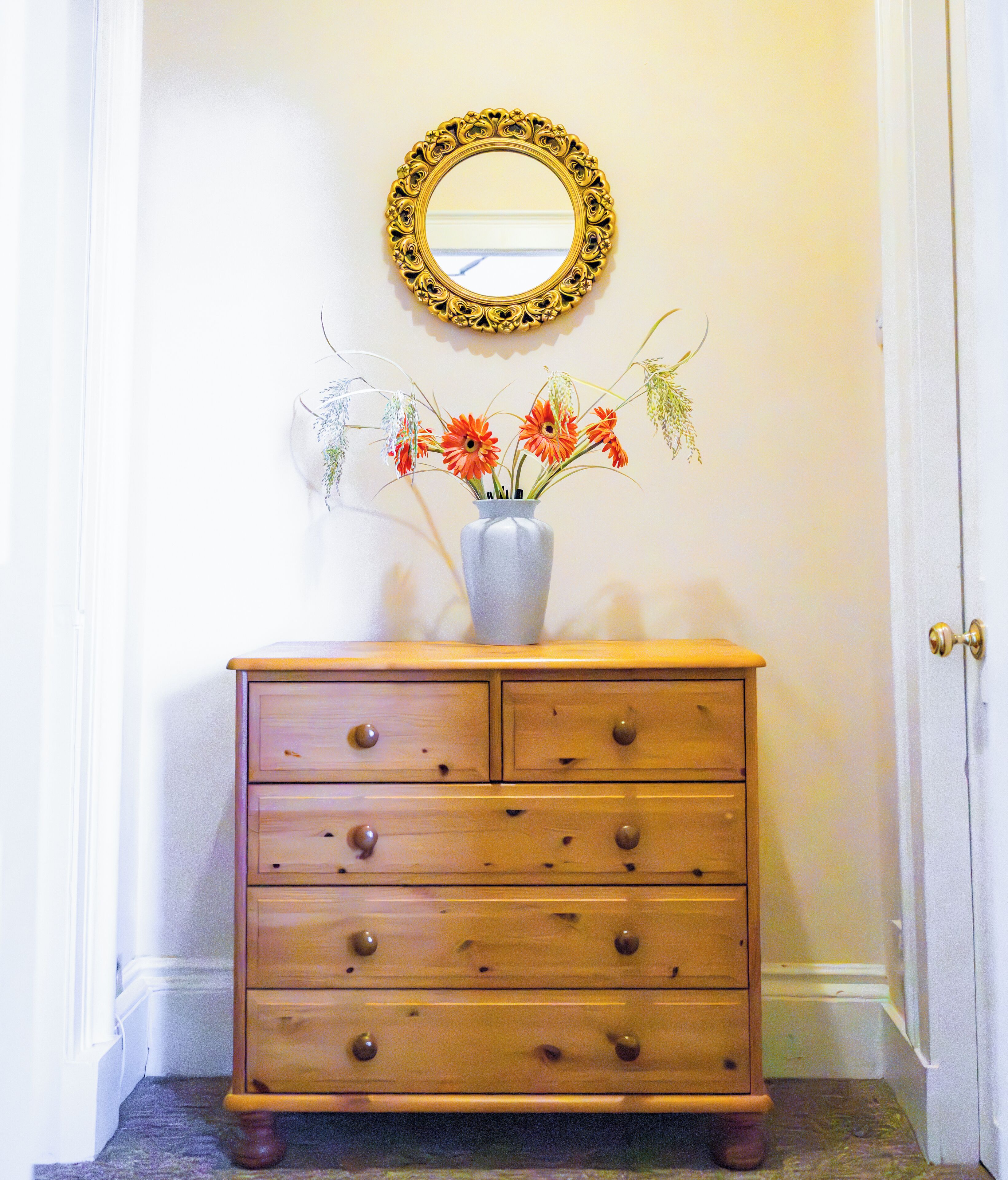 A wooden dresser with drawers and knobs, a vase with flowers, and a mirror on the wall.