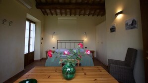 Een kamer met een houten tafel, een groene vaas met bloemen, een bed met een blauwe sprei en een stoel.