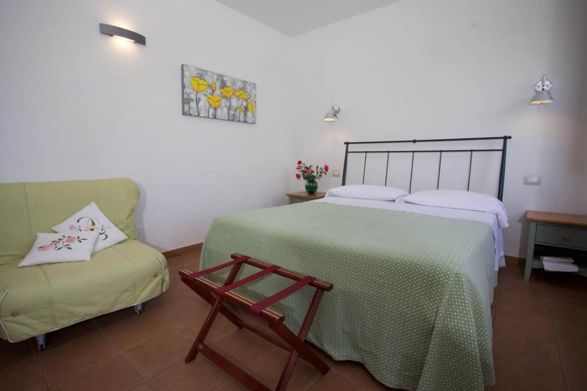Een slaapkamer met een bed, een groene bank, een houten stoel en een schilderij aan de muur.