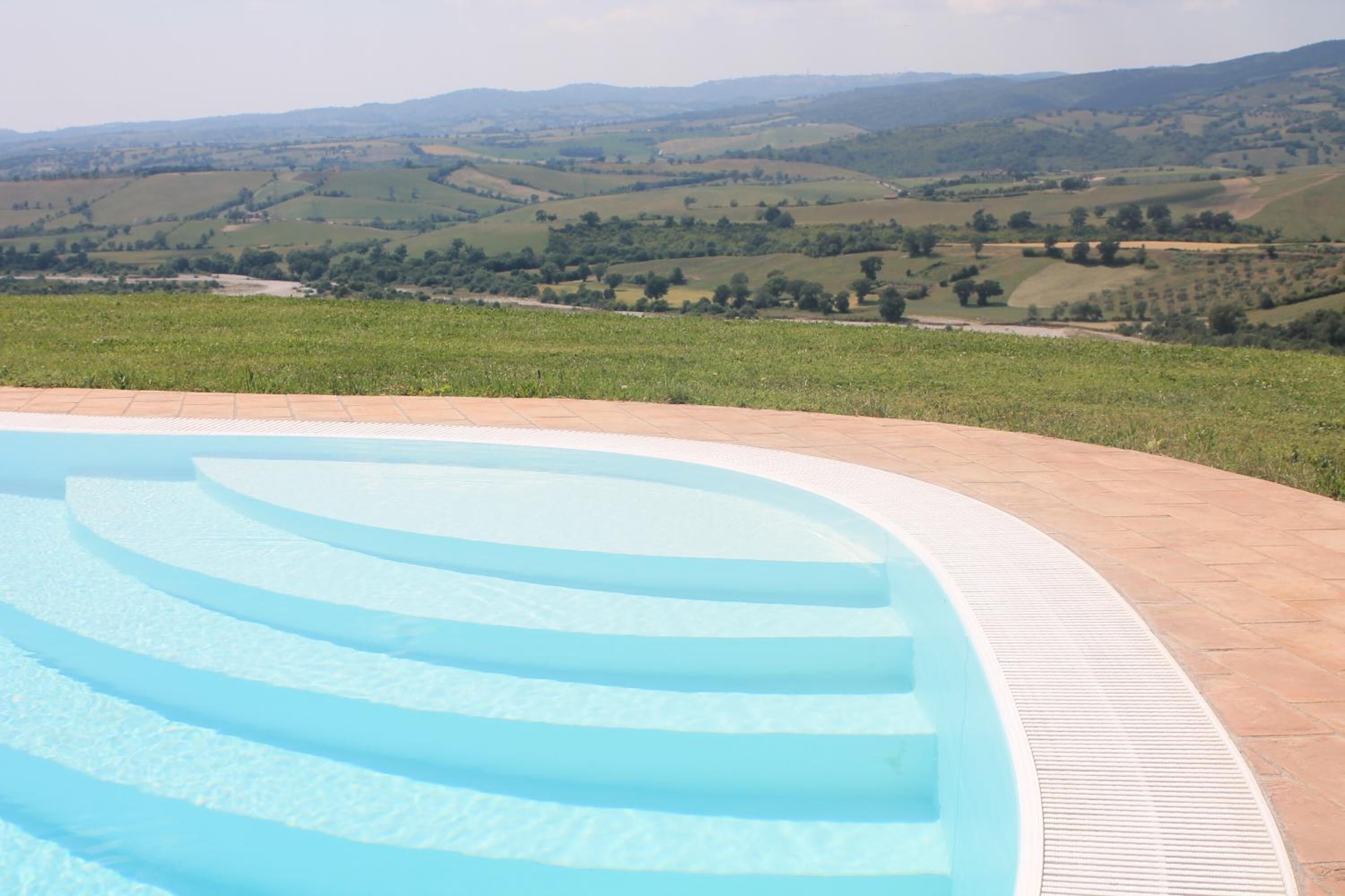 Une piscine avec des marches en gradins et une vue sur des collines verdoyantes en arrière-plan.