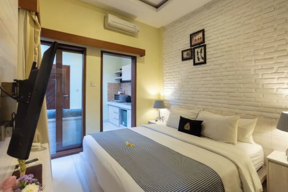 A hotel room with a bed, bedside table, lamp, and a white brick wall.