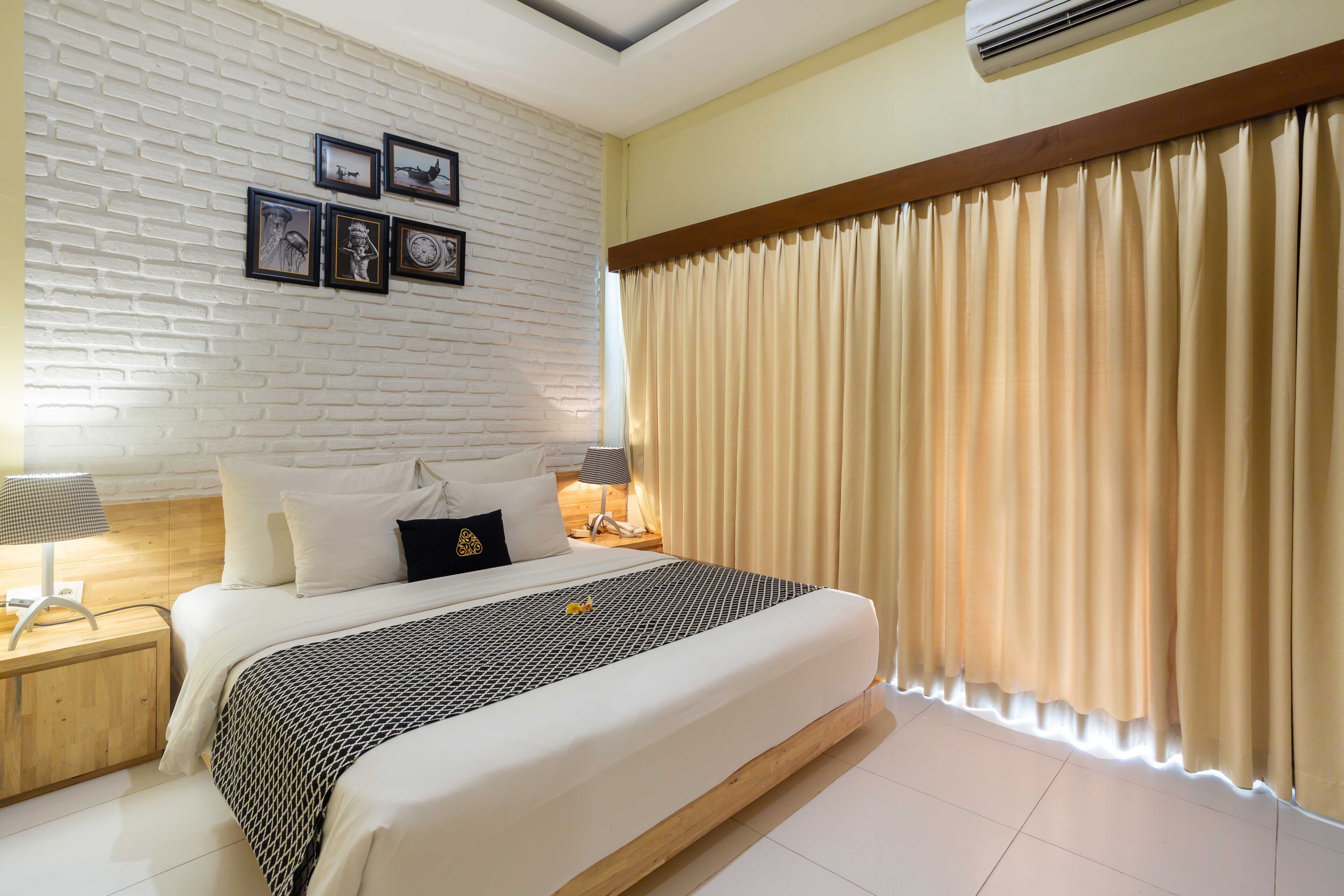Una habitación de hotel moderna con una cama grande, pared de ladrillo blanco y cuadros enmarcados.