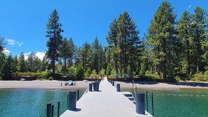 A wooden pier extending into a clear blue lake, surrounded by dense green trees.