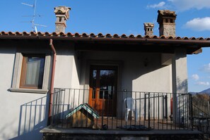 A house with a tiled roof, a wooden door, and a small porch with a railing. - Villa Farfalla Bianca (Vitorchiano)