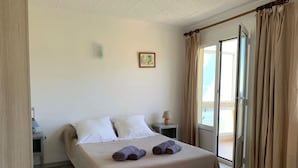 A hotel room with a bed, two bedside tables, a lamp, a picture on the wall, and a sliding glass door to the outside. - Les Asphodèles (Partinello)