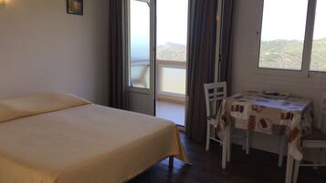 Ein Schlafzimmer mit einem Bett, einem Tisch mit Tischdecke und Blick ins Freie durch ein Fenster.