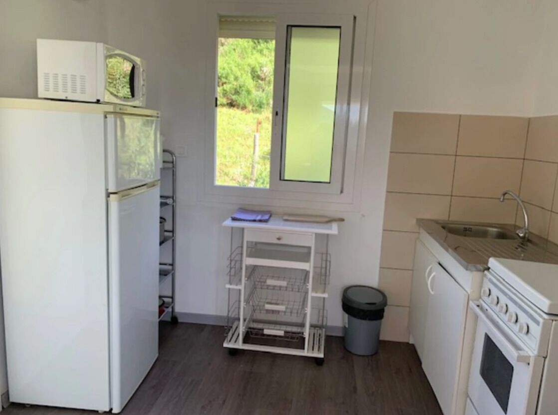 A compact kitchen with a refrigerator, microwave, stove, sink, and a small window.