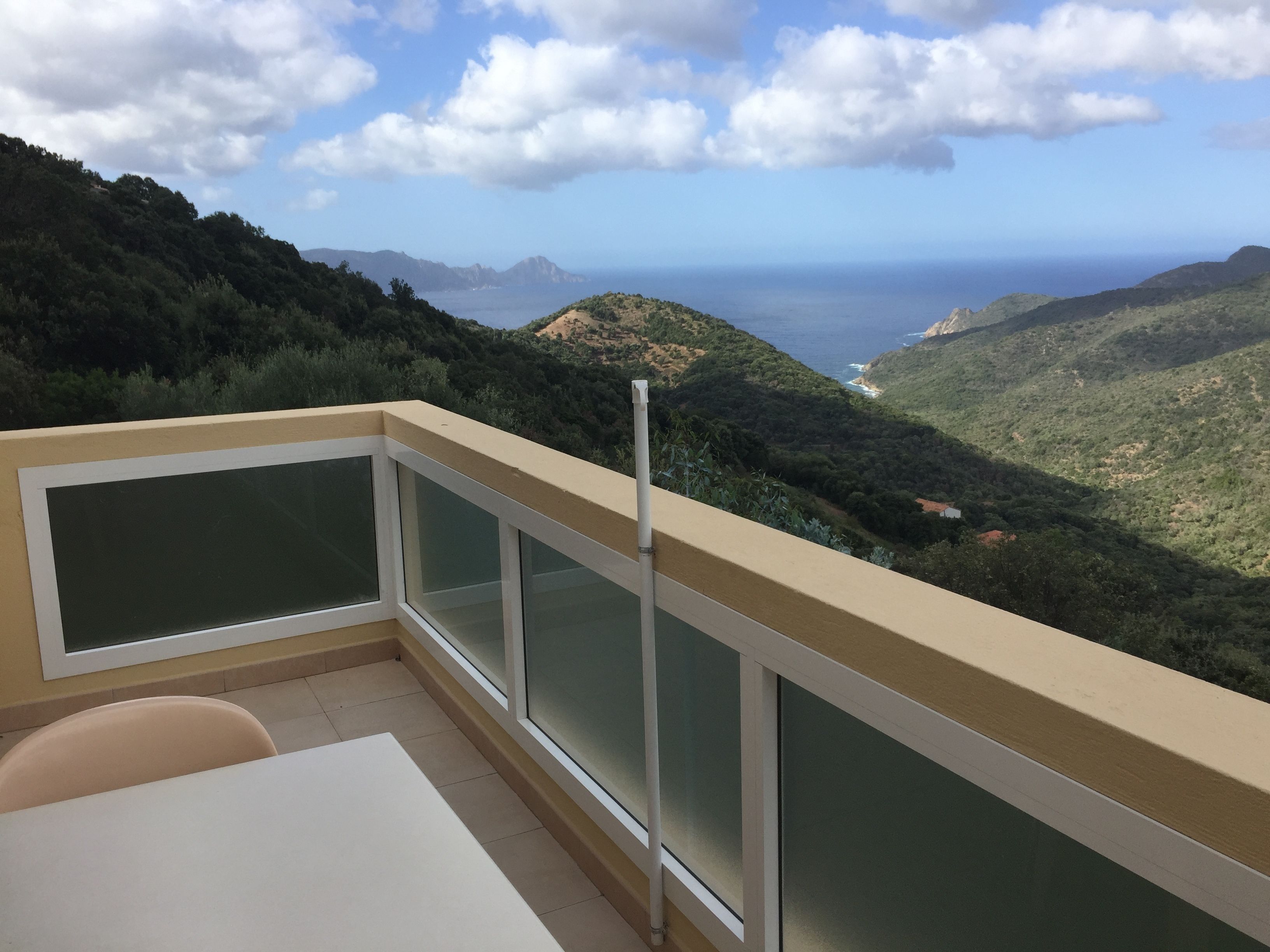 A balcony with a view of a coastal landscape, including hills and the sea.