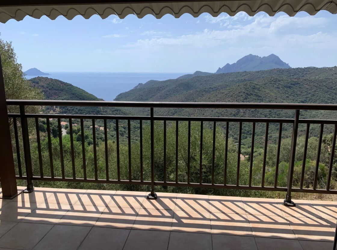A balcony with a metal railing overlooking a mountainous landscape and a body of water.