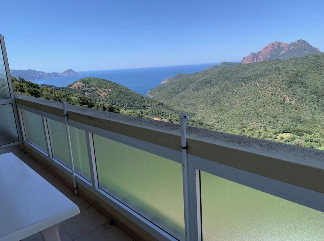 Un balcon offrant une vue sur un paysage côtier, avec des collines verdoyantes et une chaîne de montagnes lointaine.