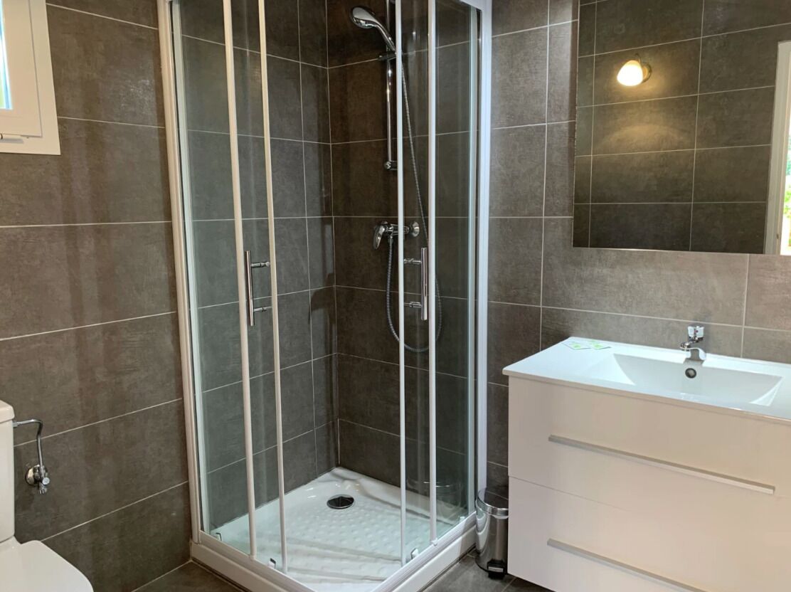 A modern bathroom with a glass-enclosed shower, a white sink, and a large mirror.